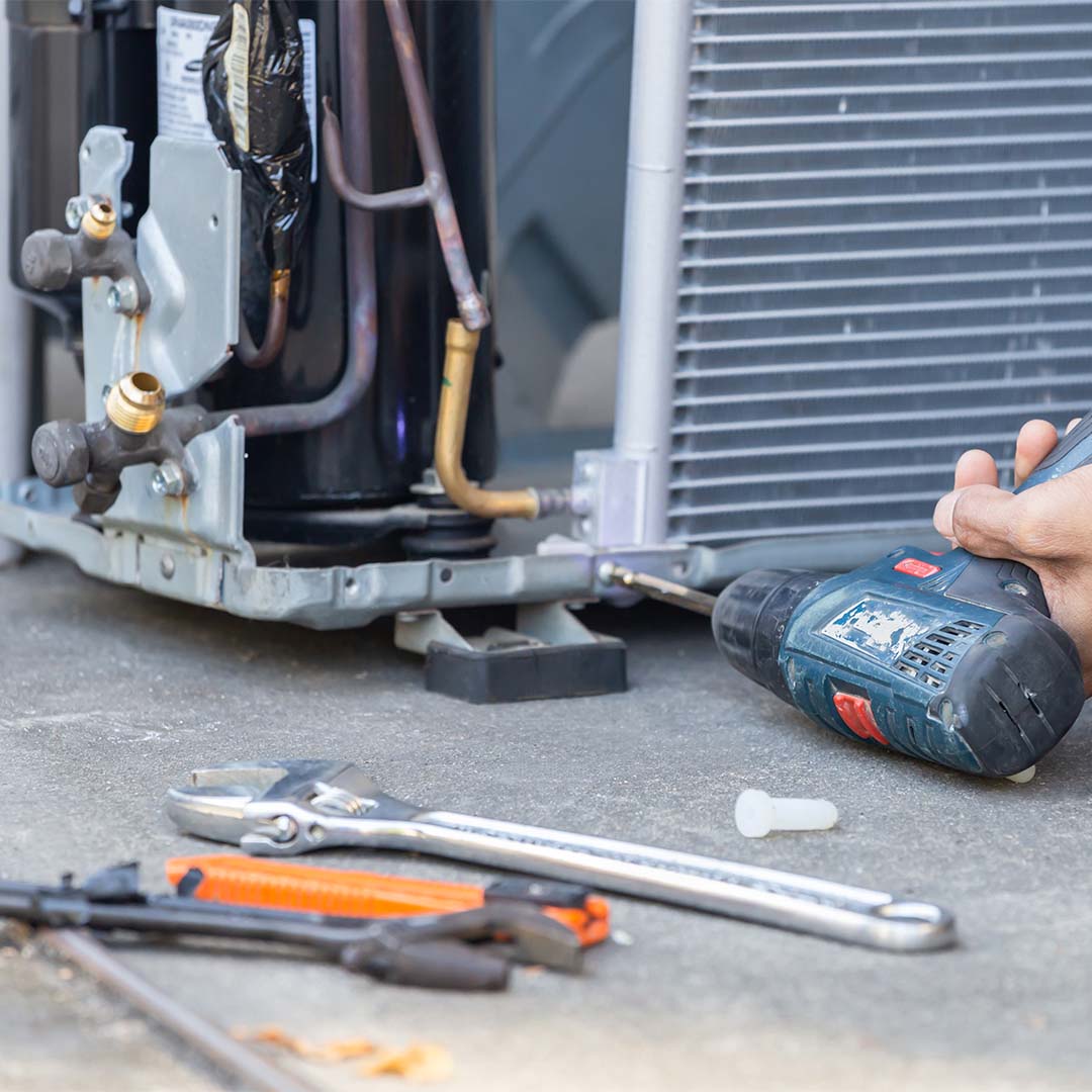Person working on a HVAC unit with tools.